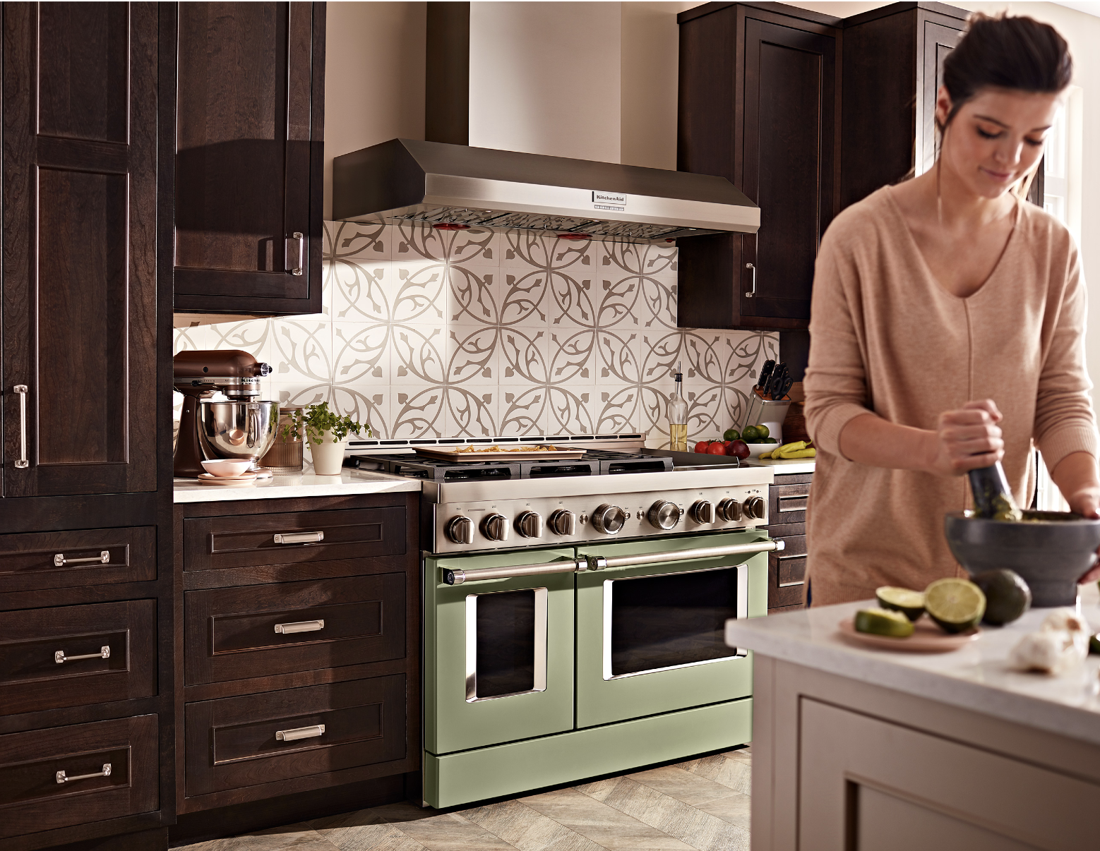 A woman using a mortar and pestal, standing in front of a professional KitchenAid gas range